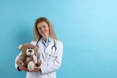Photo of Pediatrician with toy bear on light blue background. Space for text