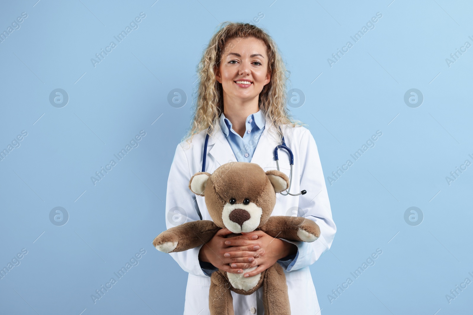 Pediatrician with toy bear on light blue background Photo of Pediatrician with toy bear on light blue background