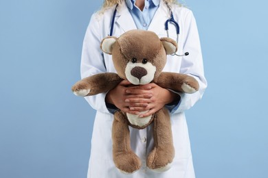 Photo of Pediatrician with toy bear on light blue background, closeup