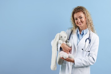 Photo of Professional pediatrician with toy bunny on light blue background. Space for text