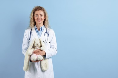 Photo of Professional pediatrician with toy bunny on light blue background. Space for text