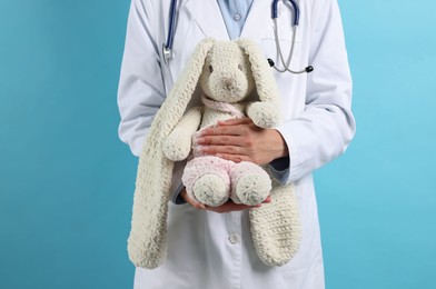 Photo of Professional pediatrician with toy bunny on light blue background, closeup