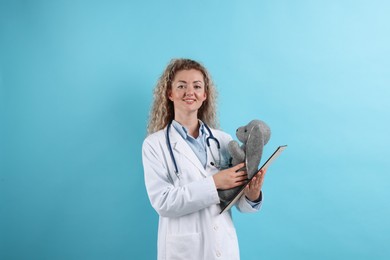 Photo of Professional pediatrician with toy bunny and clipboard on light blue background