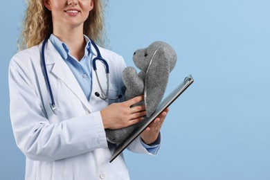 Photo of Professional pediatrician with toy bunny and clipboard on light blue background, closeup