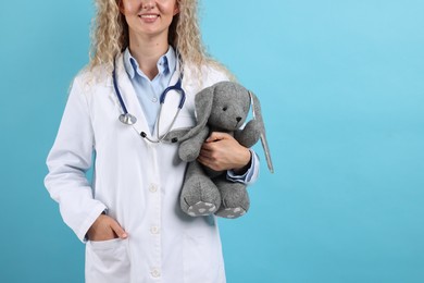 Photo of Professional pediatrician with toy bunny on light blue background, closeup. Space for text