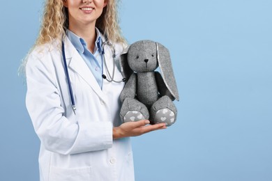 Photo of Professional pediatrician with toy bunny on light blue background, closeup. Space for text