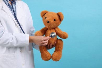 Photo of Pediatrician checking heartbeat of toy bear on light blue background, closeup. Space for text