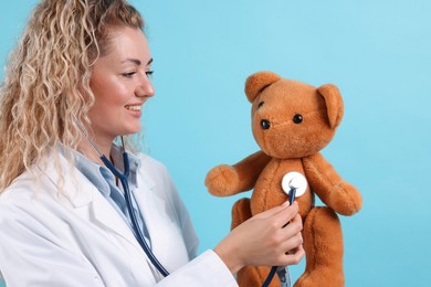 Photo of Pediatrician checking heartbeat of toy bear on light blue background