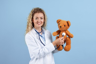 Photo of Pediatrician checking heartbeat of toy bear on light blue background