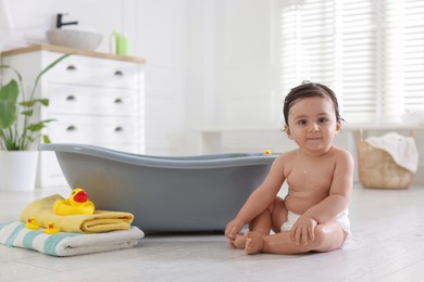 Photo of Cute little baby, towels and rubber ducks near bath at home