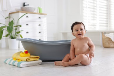 Photo of Cute little baby, towels and rubber ducks near bath at home