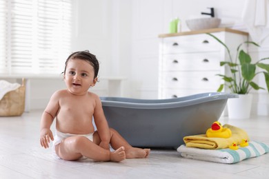 Photo of Cute little baby, towels and rubber ducks near bath at home