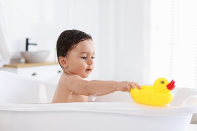 Photo of Cute little baby with rubber duck bathing in tub at home