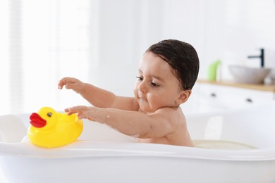 Photo of Cute little baby with rubber duck bathing in tub at home