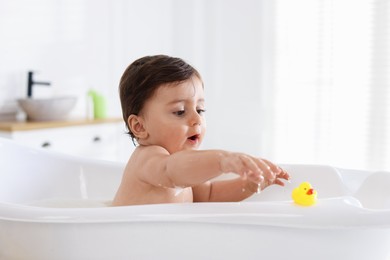 Photo of Cute little baby with rubber duck bathing in tub at home