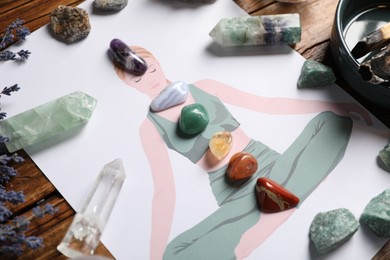 Photo of Human drawing with gemstones placed on chakras, lavender flowers on wooden table, closeup