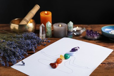Photo of Human drawing with gemstones placed on chakras, lavender flowers on wooden table, closeup