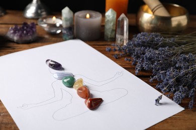 Photo of Human drawing with gemstones placed on chakras, lavender flowers on wooden table, closeup