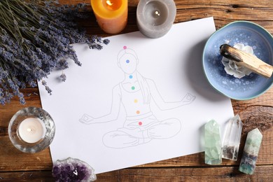 Photo of Drawing of chakras on human body, gemstones, candles, palo santo and lavender flowers on wooden table, flat lay