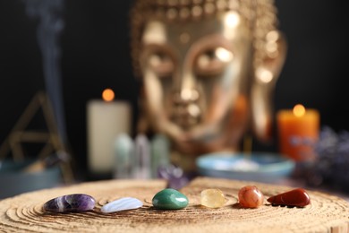 Photo of Chakra gemstones on table with candles and Buddha figure, selective focus