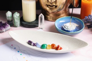 Photo of Chakra gemstones, incense and human body drawing on light pink table, closeup