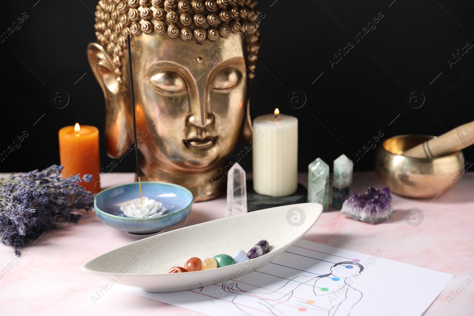 Chakra gemstones, incense, candles and Buddha figure on light pink table Photo of Chakra gemstones, incense, candles and Buddha figure on light pink table