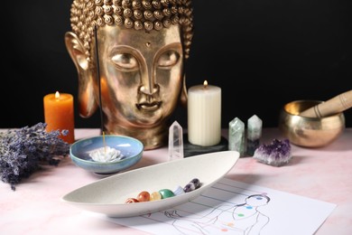 Photo of Chakra gemstones, incense, candles and Buddha figure on light pink table