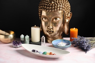 Photo of Chakra gemstones, incense, candles and Buddha figure on light pink table