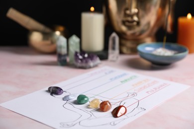 Photo of Human drawing with gemstones placed on chakras on light pink table, closeup