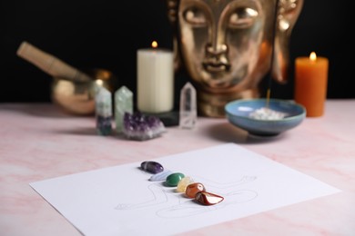 Photo of Human drawing with gemstones placed on chakras on light pink table, closeup