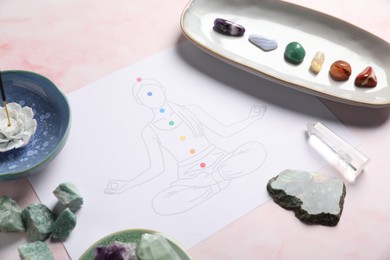 Photo of Drawing of chakras on human body, gemstones, incense on light pink table, closeup