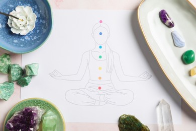 Photo of Drawing of chakras on human body, gemstones, incense on light pink table, flat lay