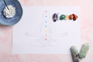 Photo of Drawing of chakras on human body, gemstones, incense on light pink table, flat lay