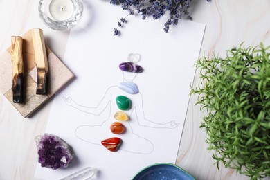 Photo of Human drawing with gemstones placed on chakras, plants and palo santo against white background, flat lay