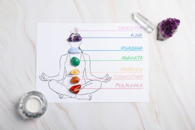 Photo of Paper sheet with chakras names and gemstones on body drawing, candle against white background, flat lay