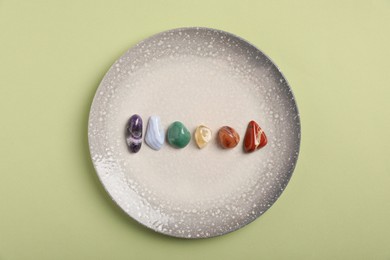 Photo of Chakra gemstones on light green background, top view