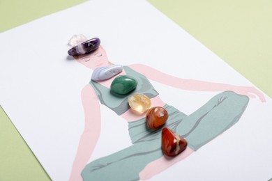 Photo of Human drawing with gemstones placed on chakras against light green background, closeup
