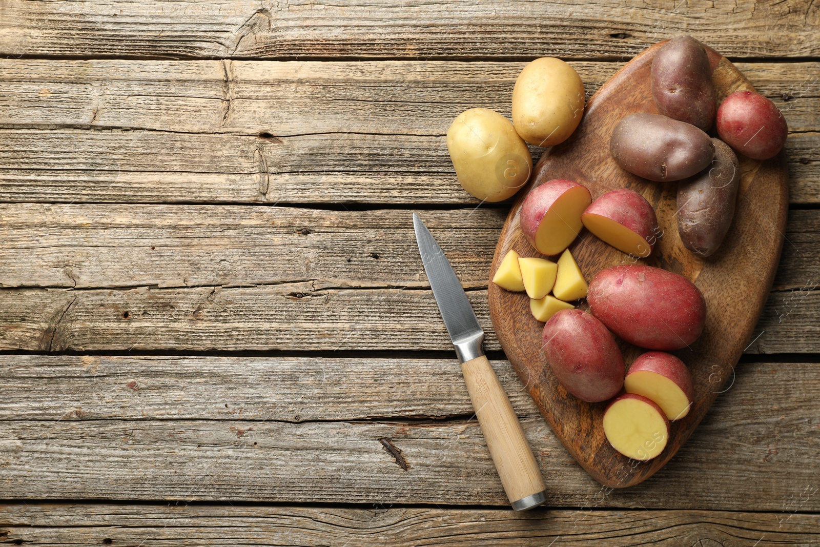 Photo of Different types of potatoes and knife on wooden table, flat lay. Space for text