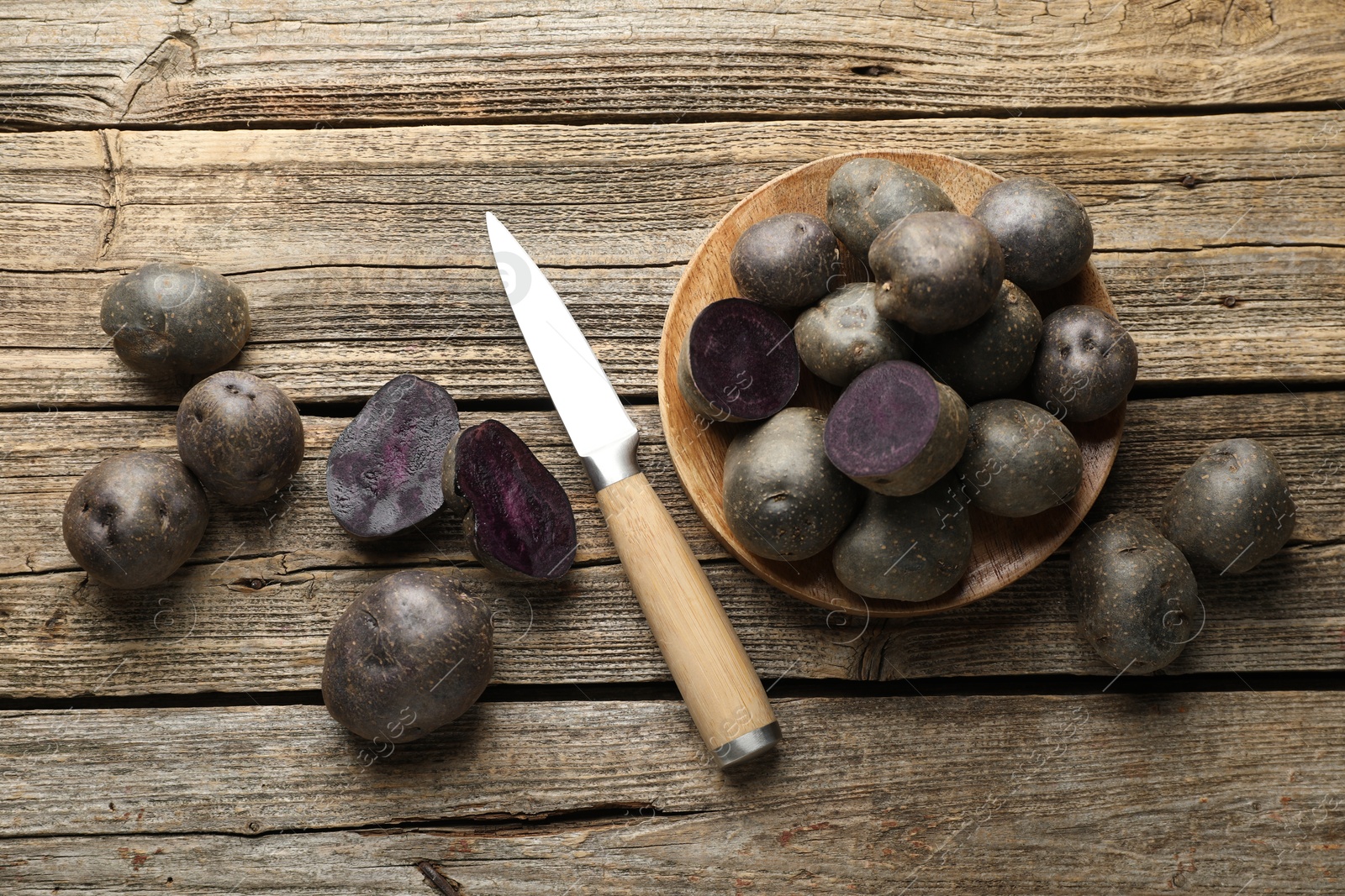 Photo of Fresh purple potatoes and knife on wooden table, flat lay