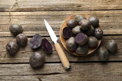 Photo of Fresh purple potatoes and knife on wooden table, flat lay