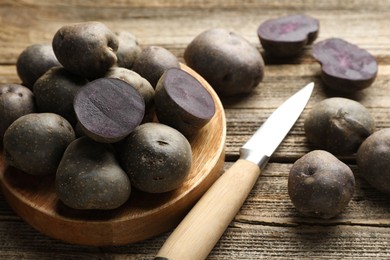 Photo of Fresh purple potatoes and knife on wooden table, closeup