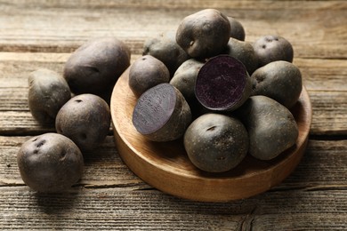 Photo of Fresh purple potatoes on wooden table, closeup