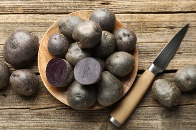 Photo of Fresh purple potatoes and knife on wooden table, flat lay