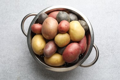 Photo of Different types of potatoes in colander on grey table, top view