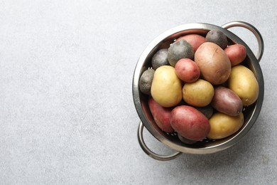 Photo of Different types of potatoes in colander on grey table, top view. Space for text