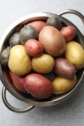 Photo of Different types of potatoes in colander on grey table, top view