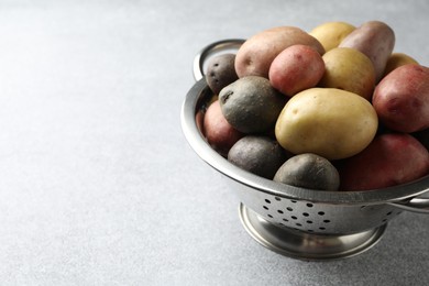 Photo of Different types of potatoes in colander on grey table, closeup. Space for text