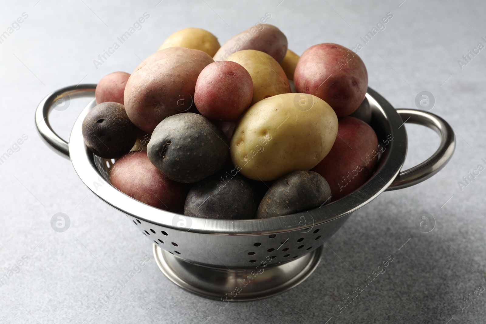 Photo of Different types of potatoes in colander on grey table, closeup