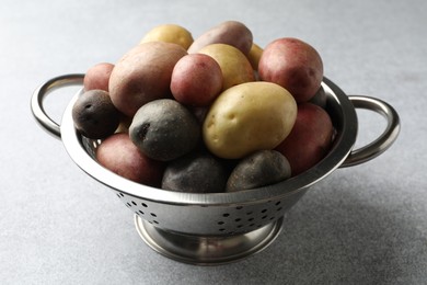 Photo of Different types of potatoes in colander on grey table, closeup