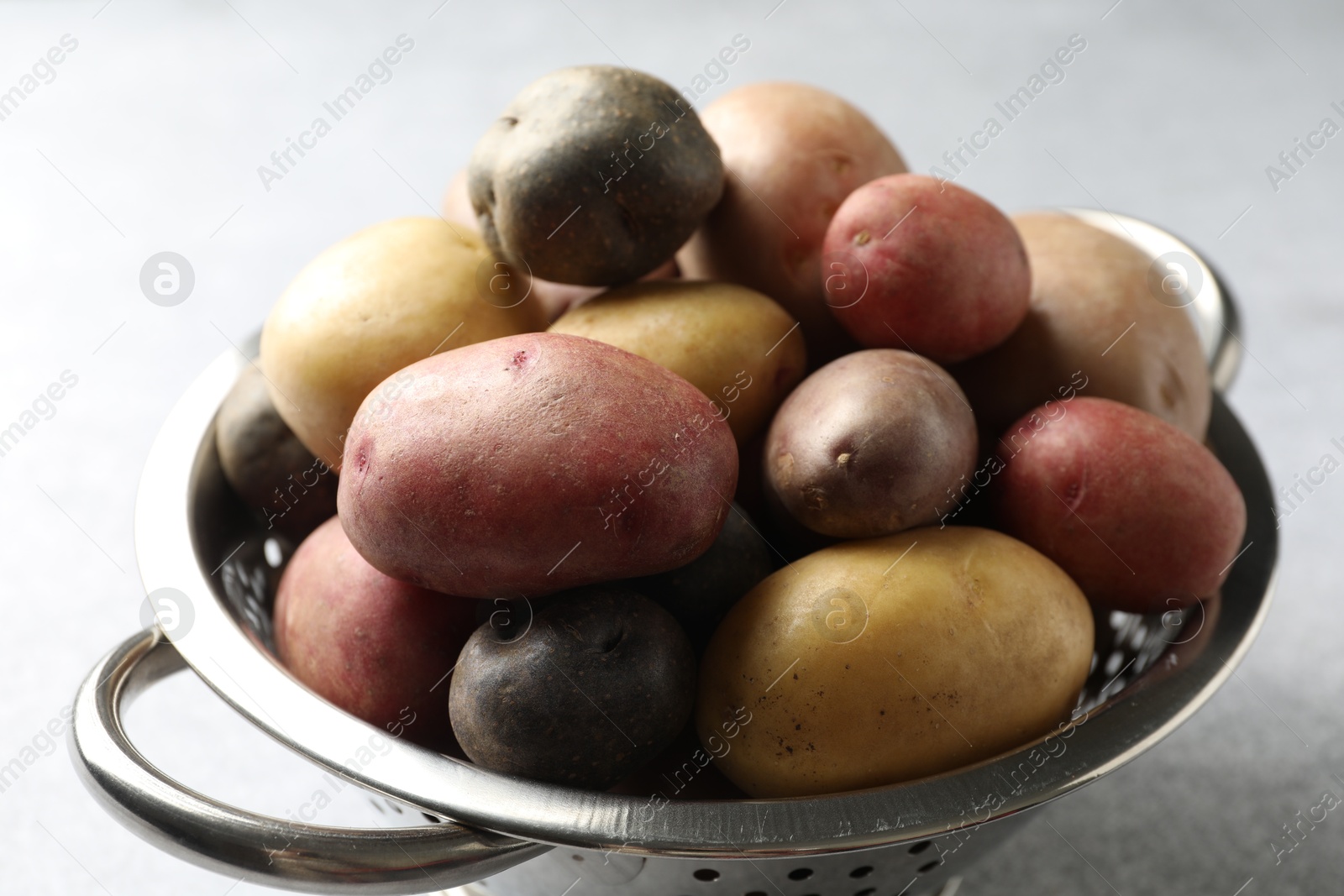 Photo of Different types of potatoes in colander on grey table, closeup